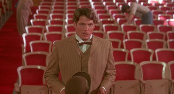 Movie still from “Somewhere in Time” (1980), directed by Jeannot Szwarc – A man in a brown suit and a hat in front of rows of red chairs; Medium shot, Over the shoulder angle
