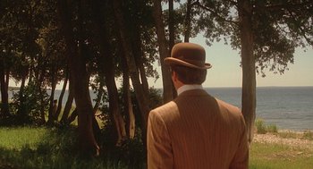 Movie still from “Somewhere in Time” (1980), directed by Jeannot Szwarc – A man wearing a suit and hat looking out at the ocean; Wide shot, Over the shoulder angle