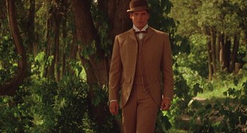 Movie still from “Somewhere in Time” (1980), directed by Jeannot Szwarc – A man in a suit and hat standing next to a tree; Medium shot, Over the shoulder angle
