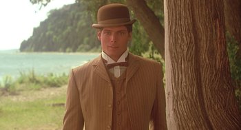 Movie still from “Somewhere in Time” (1980), directed by Jeannot Szwarc – A man wearing a suit and hat standing next to a tree in front of a body of water; Close Up shot, Low angle