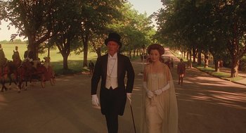 Movie still from “Somewhere in Time” (1980), directed by Jeannot Szwarc – A man and a woman dressed in formal attire walk down the street; Wide shot, High angle