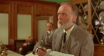 Movie still from “Somewhere in Time” (1980), directed by Jeannot Szwarc – An older man in a suit writing on a piece of paper; Close Up shot, Low angle