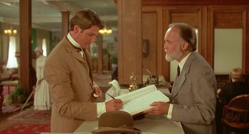 Movie still from “Somewhere in Time” (1980), directed by Jeannot Szwarc – A man in a brown suit and a man in a gray suit and a hat; Medium shot, Over the shoulder angle