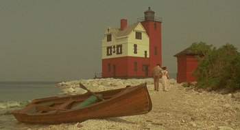 Movie still from “Somewhere in Time” (1980), directed by Jeannot Szwarc – Two people standing next to a red and white lighthouse; Extreme Wide shot, Low angle