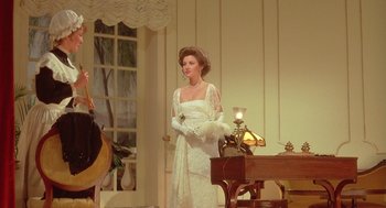 Movie still from “Somewhere in Time” (1980), directed by Jeannot Szwarc – A woman in a white dress standing in front of a table; Medium shot, Over the shoulder angle