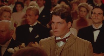 Movie still from “Somewhere in Time” (1980), directed by Jeannot Szwarc – A man in a suit and bow tie in front of a crowd; Close Up shot, Over the shoulder angle