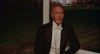 Movie still from “Somewhere in Time” (1980), directed by Jeannot Szwarc – A man in a tuxedo sitting in front of a building; Medium shot, Low angle