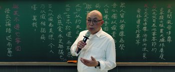 Movie still from “A Sun” (2019), directed by Mong-Hong Chung – A man holding a microphone in front of a chalkboard; Medium shot, Over the shoulder angle