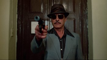 Movie still from “Sorcerer” (1977), directed by William Friedkin – A man in a hat and sunglasses holding a gun; Medium shot, Low angle