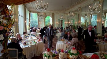 Movie still from “Sorcerer” (1977), directed by William Friedkin – A man standing in front of a group of people in a room; Wide shot, High angle