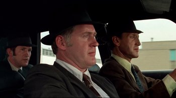 Movie still from “Sorcerer” (1977), directed by William Friedkin – A man in a suit and a man in a hat sitting in a car; Close Up shot, Low angle