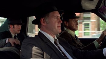 Movie still from “Sorcerer” (1977), directed by William Friedkin – Two men in suits and hats sitting in the back of a car; Medium shot, Low angle