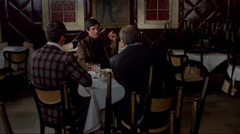 Movie still from “Sorcerer” (1977), directed by William Friedkin – A group of people sitting at a table with food; Wide shot, Over the shoulder angle
