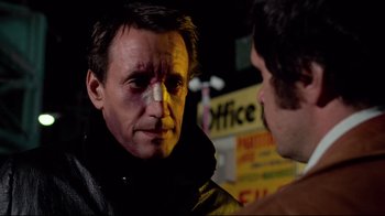 Movie still from “Sorcerer” (1977), directed by William Friedkin – A man with bruises on his face is talking to another man; Close Up shot, Over the shoulder angle