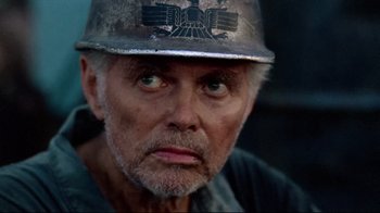 Movie still from “Sorcerer” (1977), directed by William Friedkin – An older man wearing a hard hat and looking at the camera; Close Up shot, Over the shoulder angle
