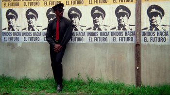 Movie still from “Sorcerer” (1977), directed by William Friedkin – A man standing in front of a wall with a poster of a man in military uniform; Medium shot, Low angle