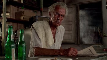 Movie still from “Sorcerer” (1977), directed by William Friedkin – An older man sitting at a table with a bottle of beer; Close Up shot, Low angle