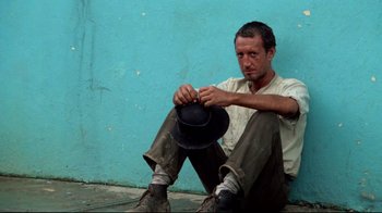 Movie still from “Sorcerer” (1977), directed by William Friedkin – A man sitting on the ground with a hat in his hand; Medium shot, Low angle