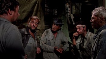 Movie still from “Sorcerer” (1977), directed by William Friedkin – A group of men standing next to each other in a room; Medium shot, Low angle