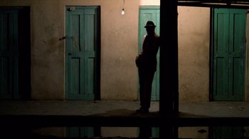 Movie still from “Sorcerer” (1977), directed by William Friedkin – A man standing in front of a building at night; Wide shot, Low angle