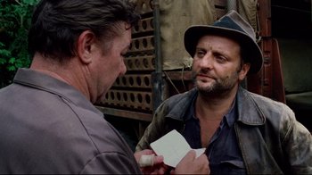 Movie still from “Sorcerer” (1977), directed by William Friedkin – A man holding a piece of paper next to another man wearing a hat; Close Up shot, Over the shoulder angle