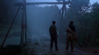 Movie still from “Sorcerer” (1977), directed by William Friedkin – A couple of men standing on top of a dirt road; Wide shot, Low angle