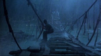 Movie still from “Sorcerer” (1977), directed by William Friedkin – A man holding onto a pole while standing on top of a wooden bridge; Wide shot, Low angle