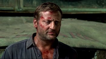 Movie still from “Sorcerer” (1977), directed by William Friedkin – A person wearing a shirt with blood all over his face; Close Up shot, Over the shoulder angle