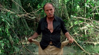 Movie still from “Sorcerer” (1977), directed by William Friedkin – An older man is holding his pants open in the woods; Medium shot, Low angle