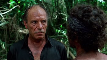 Movie still from “Sorcerer” (1977), directed by William Friedkin – A man and a woman standing next to each other in the woods; Close Up shot, Over the shoulder angle