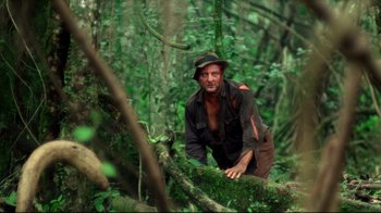 Movie still from “Sorcerer” (1977), directed by William Friedkin – A man in a hat is standing in the woods; Wide shot, Low angle
