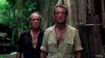 Movie still from “Sorcerer” (1977), directed by William Friedkin – Two men standing next to each other in the woods; Medium shot, Low angle