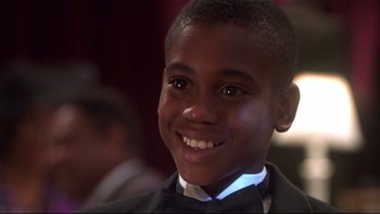 Movie still from “Soul Food” (1997), directed by George Tillman Jr. – A young boy wearing a suit and bow tie smiling; Close Up shot, Over the shoulder angle