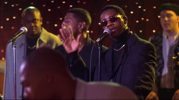 Movie still from “Soul Food” (1997), directed by George Tillman Jr. – A man in a black jacket is singing into a microphone; Medium shot, Low angle