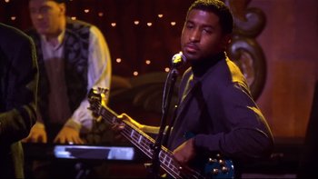 Movie still from “Soul Food” (1997), directed by George Tillman Jr. – A man holding a bass guitar while standing in front of a microphone; Medium shot, Over the shoulder angle