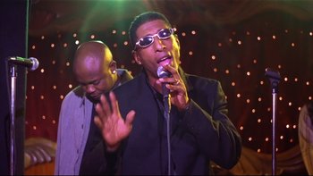 Movie still from “Soul Food” (1997), directed by George Tillman Jr. – A man singing into a microphone while another man watches; Medium shot, Low angle