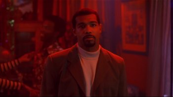 Movie still from “Soul Food” (1997), directed by George Tillman Jr. – A man in a suit standing in front of a red wall; Medium shot, Low angle