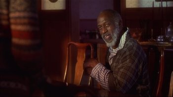 Movie still from “Soul Food” (1997), directed by George Tillman Jr. – An older man sitting at a table in a room; Medium shot, Over the shoulder angle