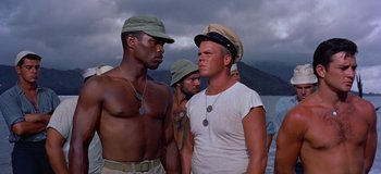 Movie still from “South Pacific” (1958), directed by Joshua Logan – A group of men standing next to each other on a beach; Medium shot, Low angle