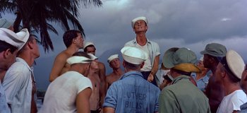 Movie still from “South Pacific” (1958), directed by Joshua Logan – A group of men standing next to each other on a beach; Medium shot, Low angle
