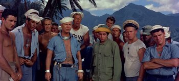 Movie still from “South Pacific” (1958), directed by Joshua Logan – A group of men standing next to each other in front of some mountains; Medium shot, High angle