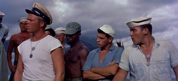 Movie still from “South Pacific” (1958), directed by Joshua Logan – A group of men standing next to each other on a beach; Medium shot, Low angle