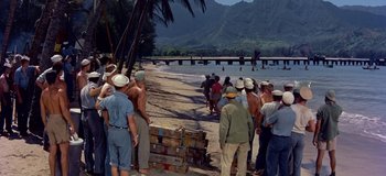 Movie still from “South Pacific” (1958), directed by Joshua Logan – A group of people standing on a beach near a body of water; Extreme Wide shot, High angle