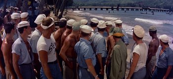 Movie still from “South Pacific” (1958), directed by Joshua Logan – A group of men standing next to each other on a beach; Wide shot, High angle