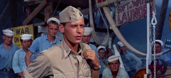 Movie still from “South Pacific” (1958), directed by Joshua Logan – A man wearing a hat standing in front of a group of sailors; Medium shot, Low angle