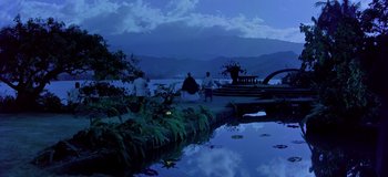Movie still from “South Pacific” (1958), directed by Joshua Logan – A group of people sitting on a bench next to a body of water; Extreme Wide shot, High angle