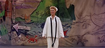 Movie still from “South Pacific” (1958), directed by Joshua Logan – A woman in a sailor suit standing in front of a mural; Medium shot, Low angle