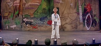Movie still from “South Pacific” (1958), directed by Joshua Logan – A man in a karate outfit stands on a stage; Wide shot, Over the shoulder angle