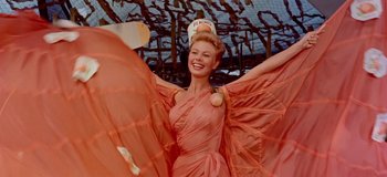 Movie still from “South Pacific” (1958), directed by Joshua Logan – A beautiful woman in a pink dress posing for a picture; Medium shot, Low angle