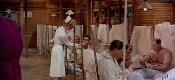 Movie still from “South Pacific” (1958), directed by Joshua Logan – A woman in a nurse's uniform standing in front of a group of men; Wide shot, High angle